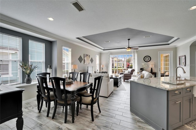 dining room with a tray ceiling, visible vents, crown molding, and wood tiled floor