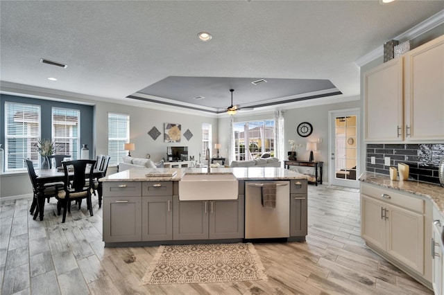 kitchen with light stone counters, a tray ceiling, stainless steel dishwasher, open floor plan, and a sink