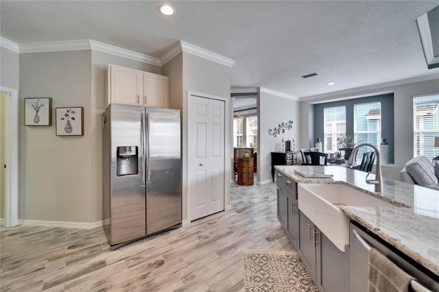 kitchen featuring appliances with stainless steel finishes, ornamental molding, light wood-style floors, white cabinetry, and a sink