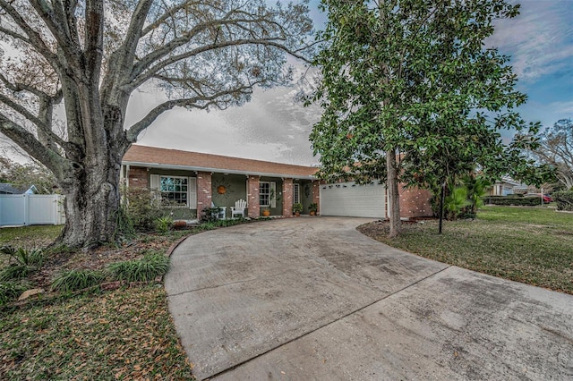 ranch-style home featuring an attached garage, brick siding, fence, concrete driveway, and a front yard