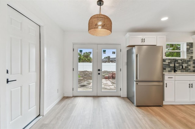 kitchen with white cabinets, decorative backsplash, freestanding refrigerator, light wood-type flooring, and a sink