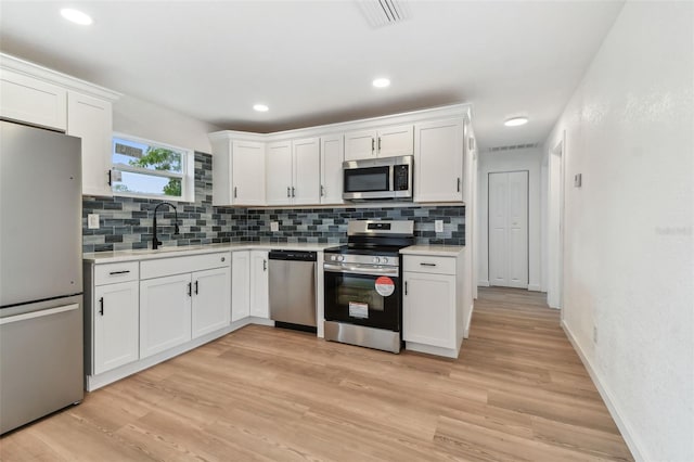 kitchen with stainless steel appliances, light countertops, light wood-type flooring, white cabinetry, and a sink