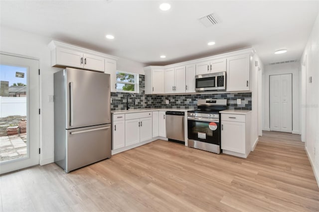 kitchen with stainless steel appliances, light countertops, white cabinetry, and light wood-style floors