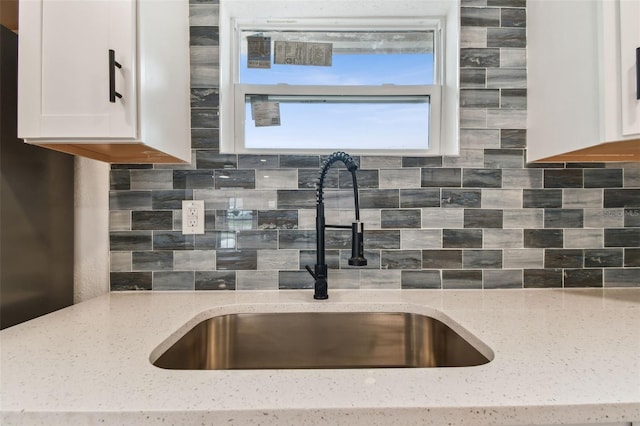 kitchen with tasteful backsplash, a sink, light stone counters, and white cabinetry