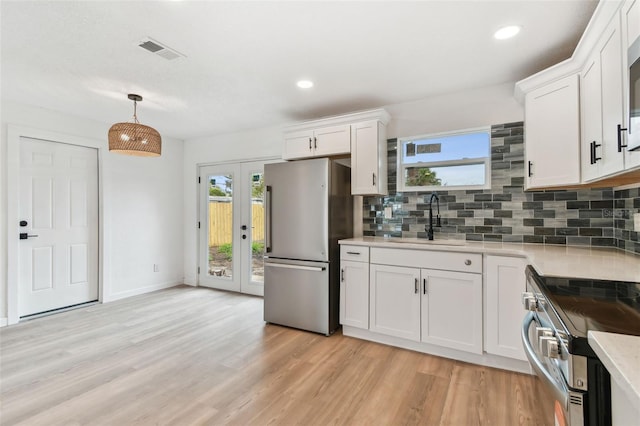 kitchen with visible vents, light wood-style flooring, a sink, stainless steel appliances, and backsplash