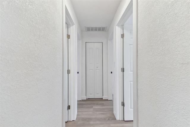 hallway with visible vents, a textured wall, and wood finished floors