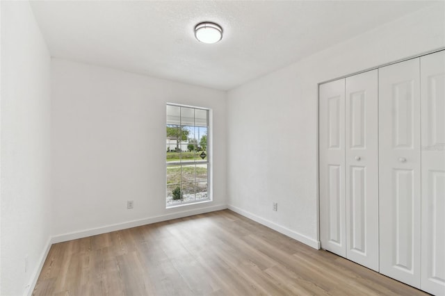 unfurnished bedroom featuring a textured ceiling, a closet, light wood-style flooring, and baseboards