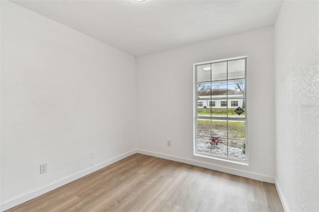 spare room featuring light wood-type flooring, a textured wall, and baseboards