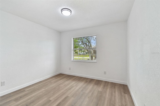 empty room with a textured wall, a textured ceiling, baseboards, and wood finished floors