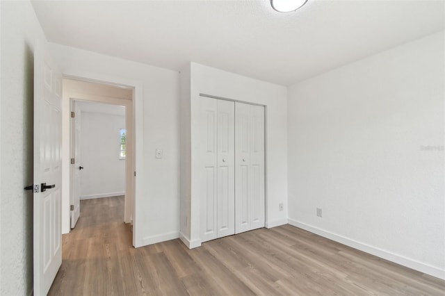 unfurnished bedroom featuring light wood finished floors, baseboards, and a closet