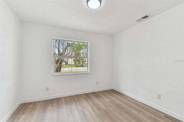 spare room featuring a textured ceiling, light wood-type flooring, visible vents, and baseboards