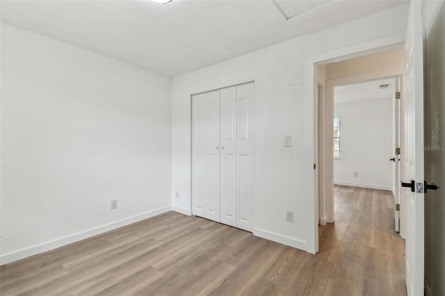 unfurnished bedroom featuring light wood finished floors, a closet, and baseboards