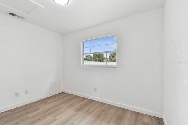 spare room with attic access, visible vents, baseboards, and wood finished floors