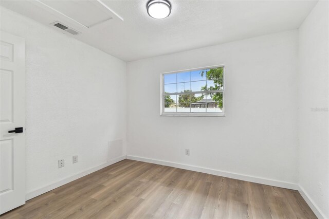 spare room featuring baseboards, attic access, visible vents, and wood finished floors