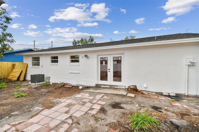 rear view of property featuring french doors, roof with shingles, stucco siding, central AC unit, and fence