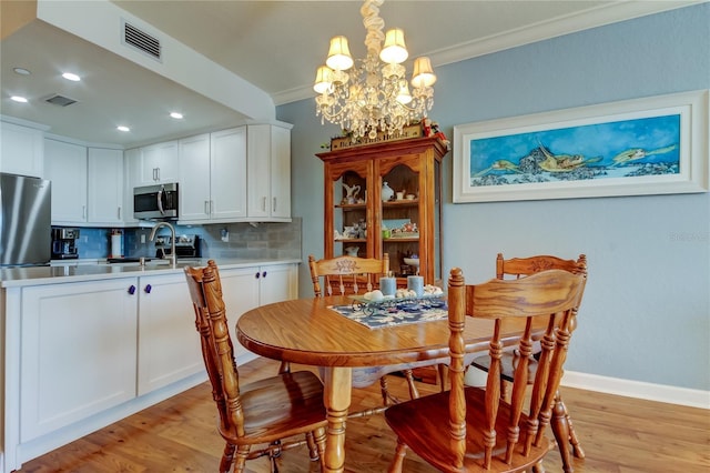 dining room featuring crown molding, light wood-type flooring, visible vents, and a chandelier