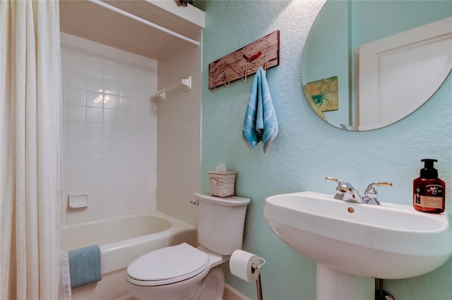 full bath with a sink, shower / bathtub combination with curtain, toilet, and a textured wall