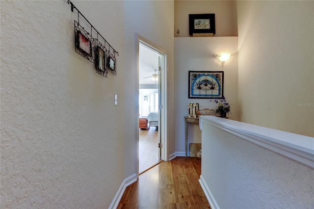 hall featuring a textured wall, baseboards, and wood finished floors