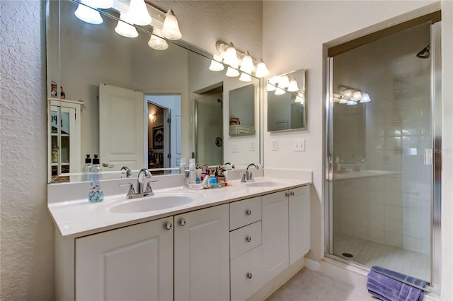 full bathroom with tile patterned flooring, double vanity, a stall shower, and a sink