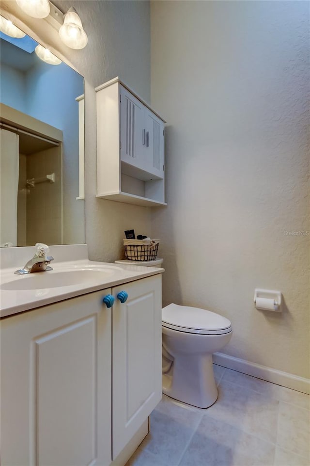 bathroom with vanity, baseboards, tile patterned floors, toilet, and a textured wall