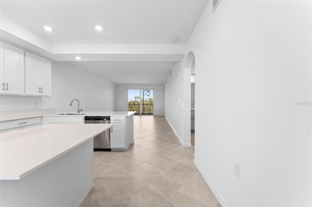 kitchen with light countertops, a peninsula, stainless steel dishwasher, white cabinetry, and a sink