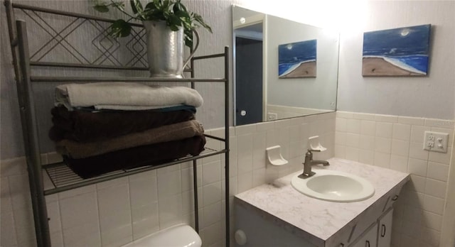 half bath with toilet, wainscoting, tile walls, and vanity