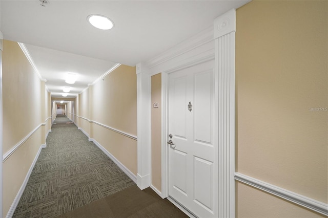 hallway with baseboards, dark colored carpet, and crown molding