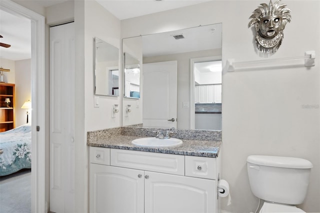 ensuite bathroom with visible vents, connected bathroom, toilet, vanity, and a closet