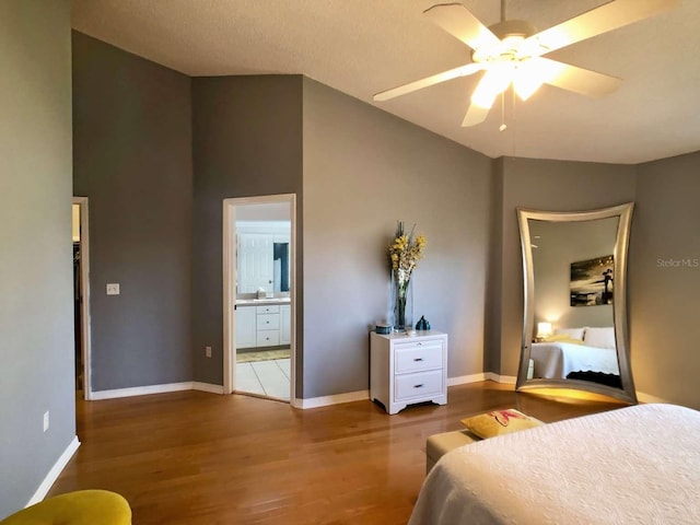 bedroom with baseboards, ceiling fan, wood finished floors, ensuite bathroom, and a sink