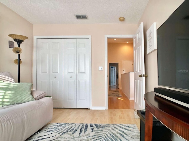 interior space with a textured ceiling, light wood-style flooring, a closet, and visible vents