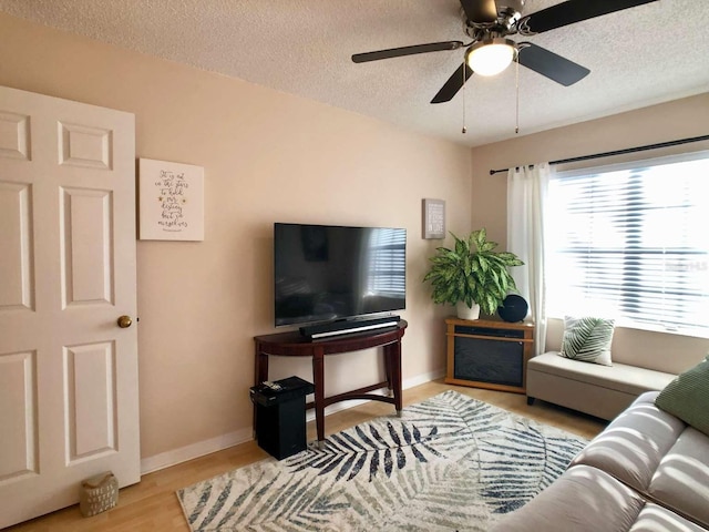 living area with light wood finished floors, ceiling fan, baseboards, and a textured ceiling