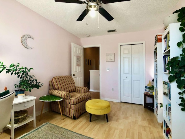 living area featuring baseboards, light wood-style flooring, visible vents, and a textured ceiling