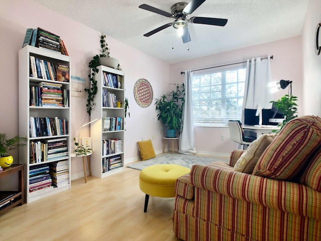 sitting room featuring a ceiling fan, light wood-style flooring, baseboards, and a textured ceiling