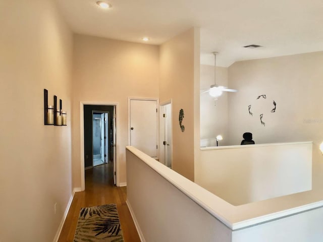 corridor with baseboards, visible vents, an upstairs landing, and wood finished floors