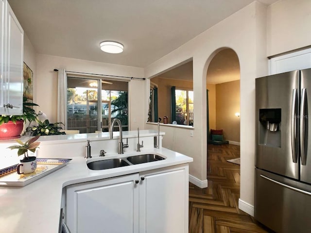 kitchen with arched walkways, a sink, white cabinets, light countertops, and stainless steel fridge