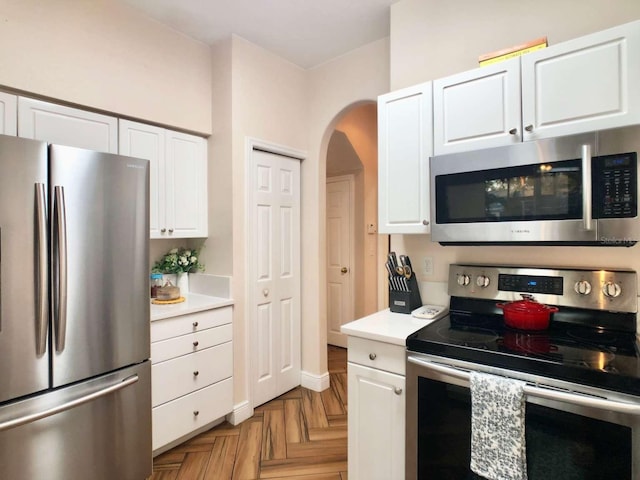 kitchen with appliances with stainless steel finishes, arched walkways, light countertops, and white cabinetry