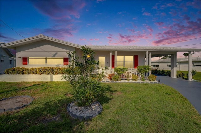 ranch-style house featuring a carport, covered porch, a yard, and driveway