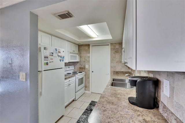 kitchen with white appliances, a sink, visible vents, white cabinets, and a raised ceiling