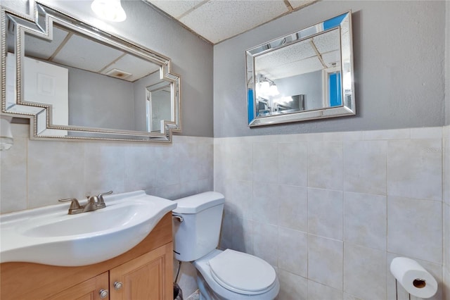 half bath with tile walls, a paneled ceiling, vanity, and toilet