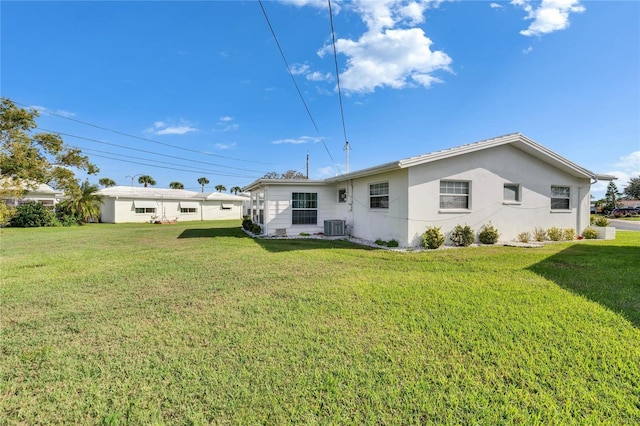 rear view of property featuring stucco siding, cooling unit, and a yard