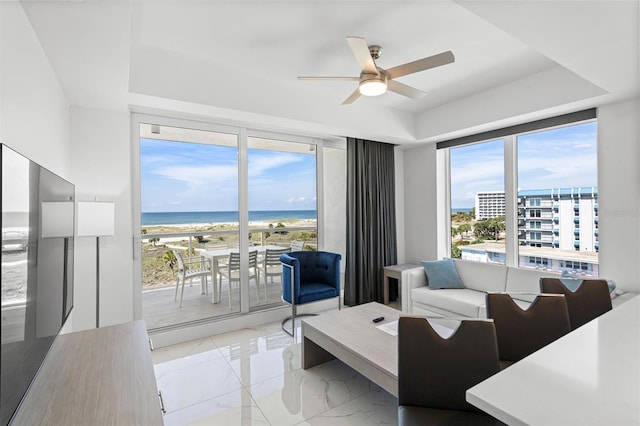 living area with a water view, marble finish floor, a tray ceiling, and a ceiling fan