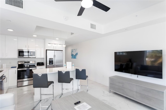 kitchen featuring a tray ceiling, marble finish floor, a breakfast bar area, stainless steel appliances, and visible vents