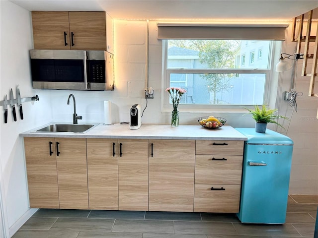 kitchen featuring stainless steel microwave, light countertops, a sink, and light brown cabinetry