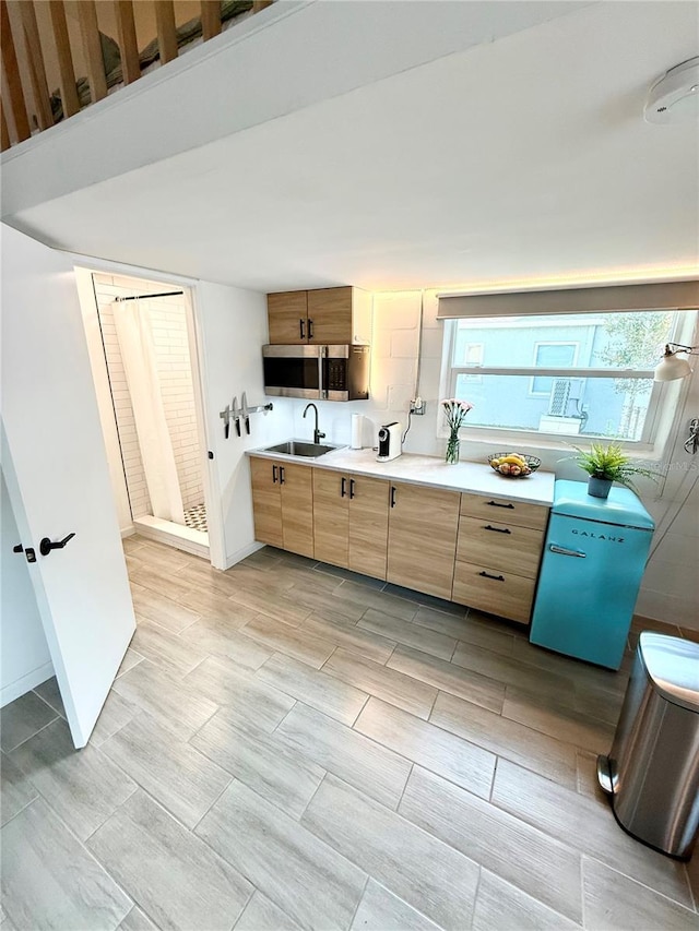 kitchen featuring baseboards, stainless steel microwave, light countertops, light brown cabinets, and a sink