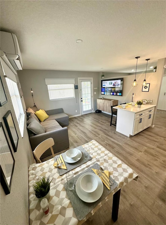 living room with a wall mounted air conditioner, a textured ceiling, baseboards, and wood finished floors