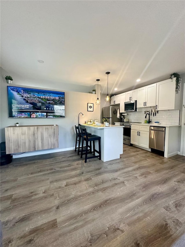 kitchen featuring wood finished floors, white cabinets, appliances with stainless steel finishes, backsplash, and decorative light fixtures