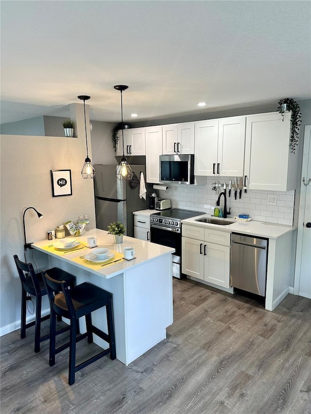 kitchen with tasteful backsplash, wood finished floors, stainless steel appliances, white cabinetry, and a sink