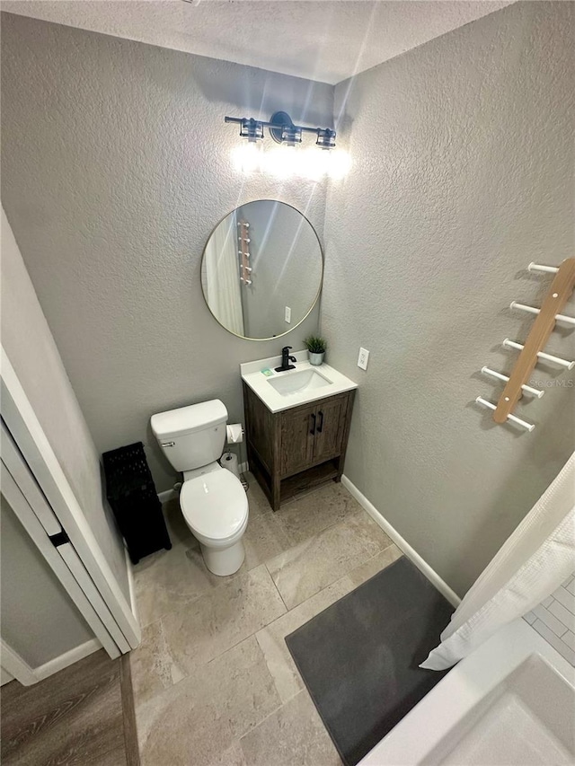 bathroom with toilet, baseboards, and a textured wall