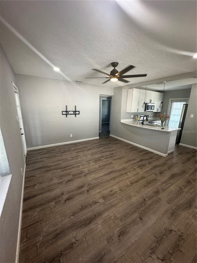 unfurnished living room with dark wood-type flooring, a textured ceiling, baseboards, and a ceiling fan