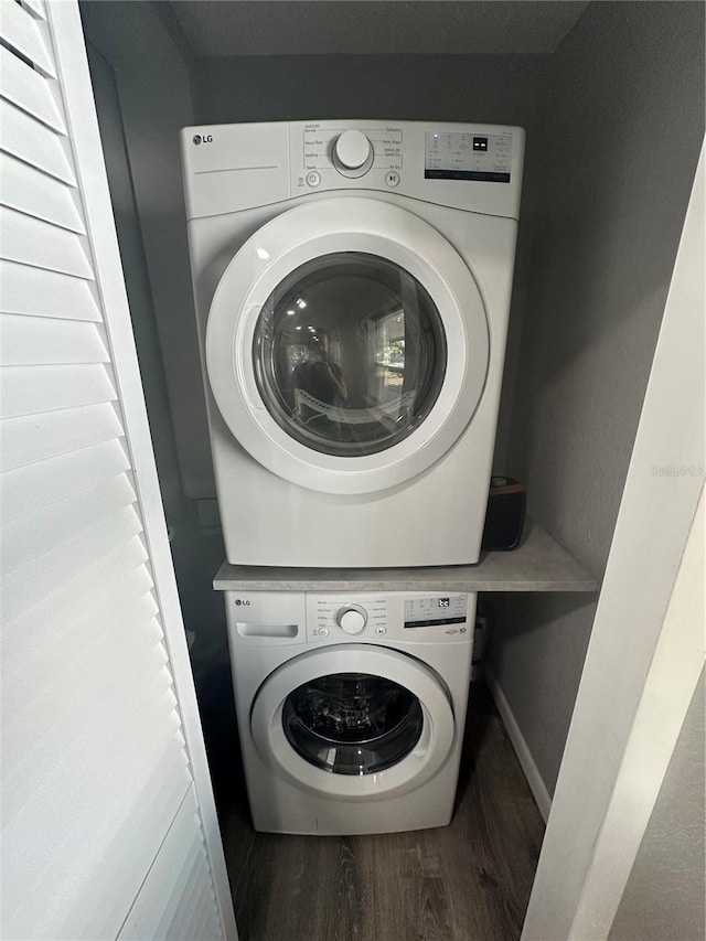 clothes washing area with baseboards, laundry area, wood finished floors, and stacked washer / drying machine